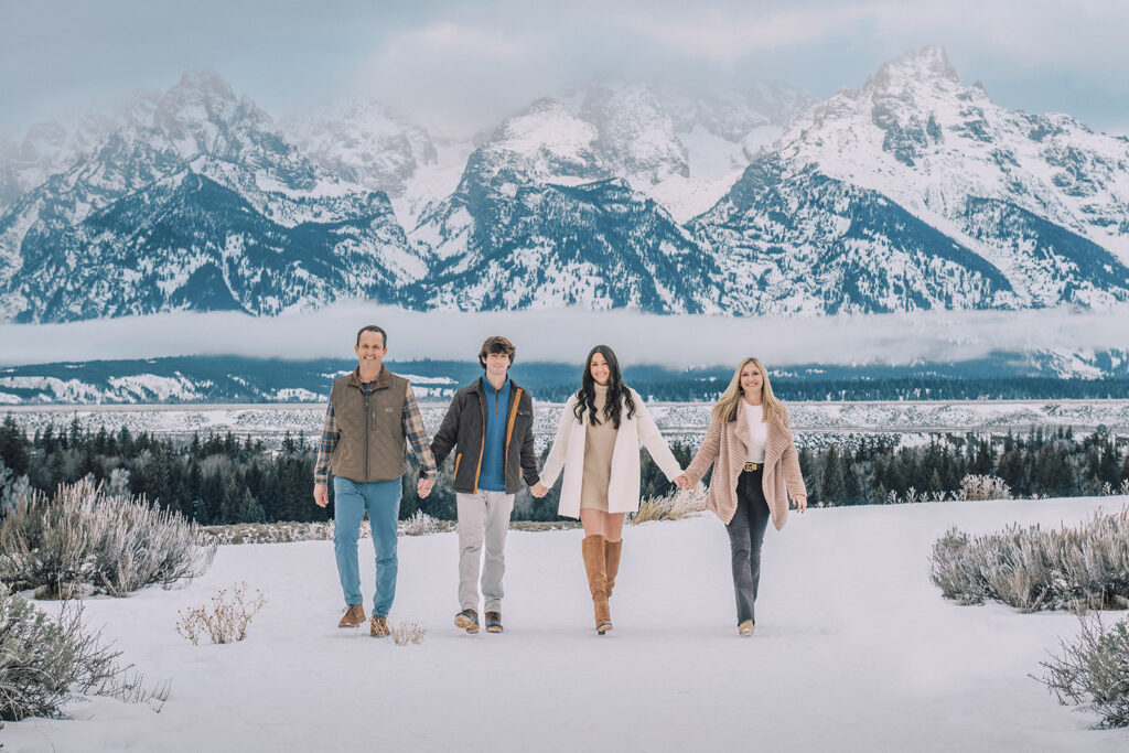 family holding hands in winter outfits in a snowy Jackson Hole landscape, outdoor winter family photo outfits, neutral palate outfit inspiration