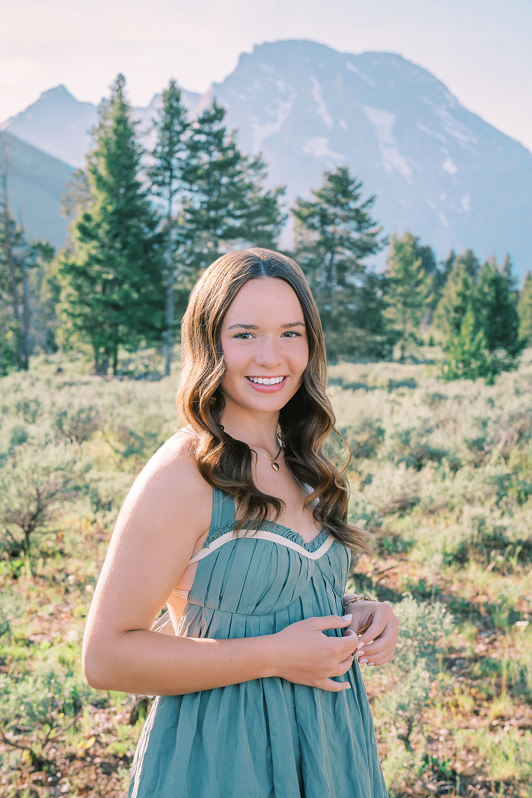 A smiling high school senior in a green dress walking in a meadow at sunrise