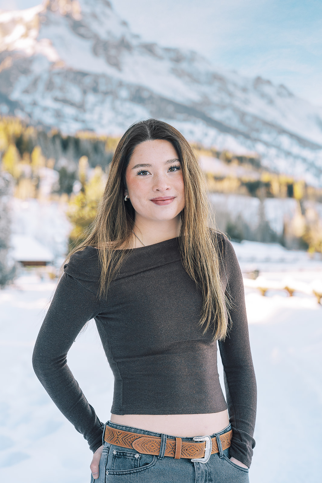 A high school grad who took advantage of test prep in Jackson, WY in a dark top and jeans smiles with a hand in her pocket in a snow covered valley