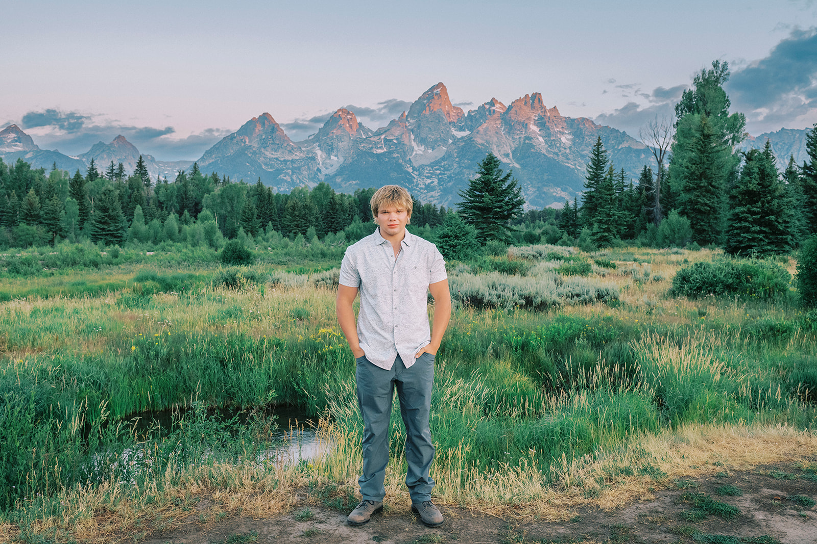 A high school senior stands with hands in pockets on a trail with the tetons behind him at sunrise after finding tutoring in Jackson, WY