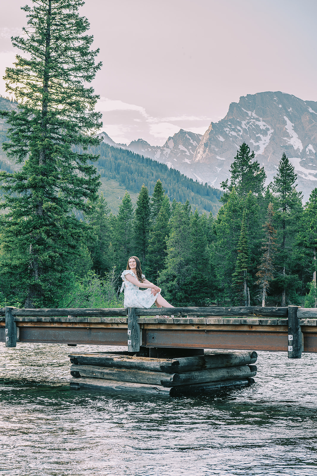 A high school senior sits on a wooden dock over the water in the mountains after finding great hair salons in Jackson, WY