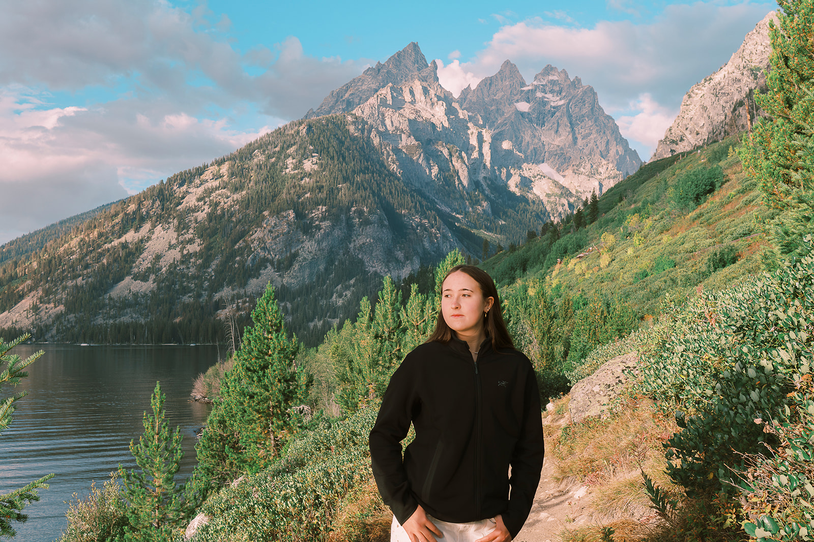 A high school grad stands gazing out at an alpine lake in a black sweater in a trail after finding test prep in Jackson, WY