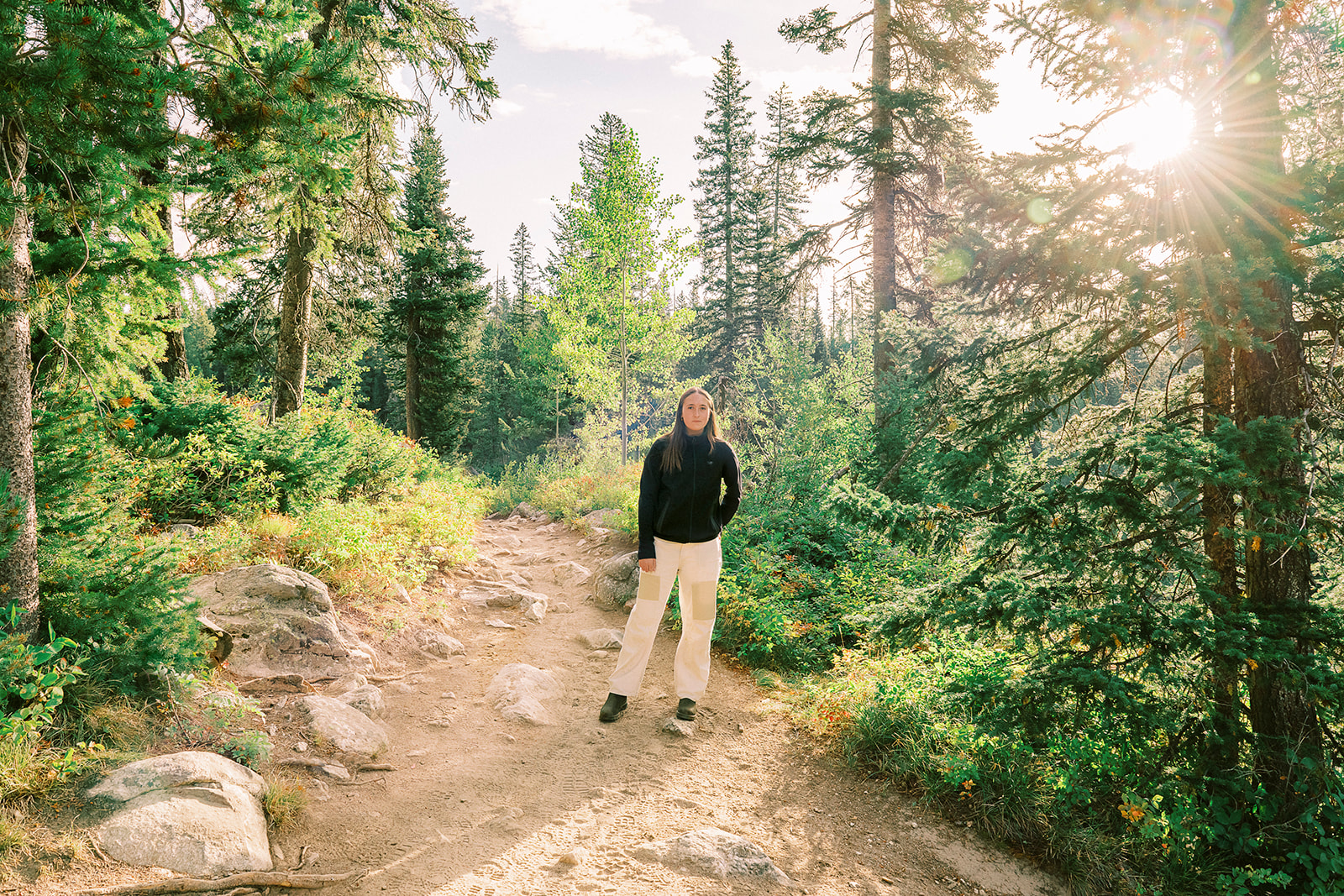 A high school senior in a black sweater stands in a mountain trail at sunset after enjoying test prep in Jackson, WY