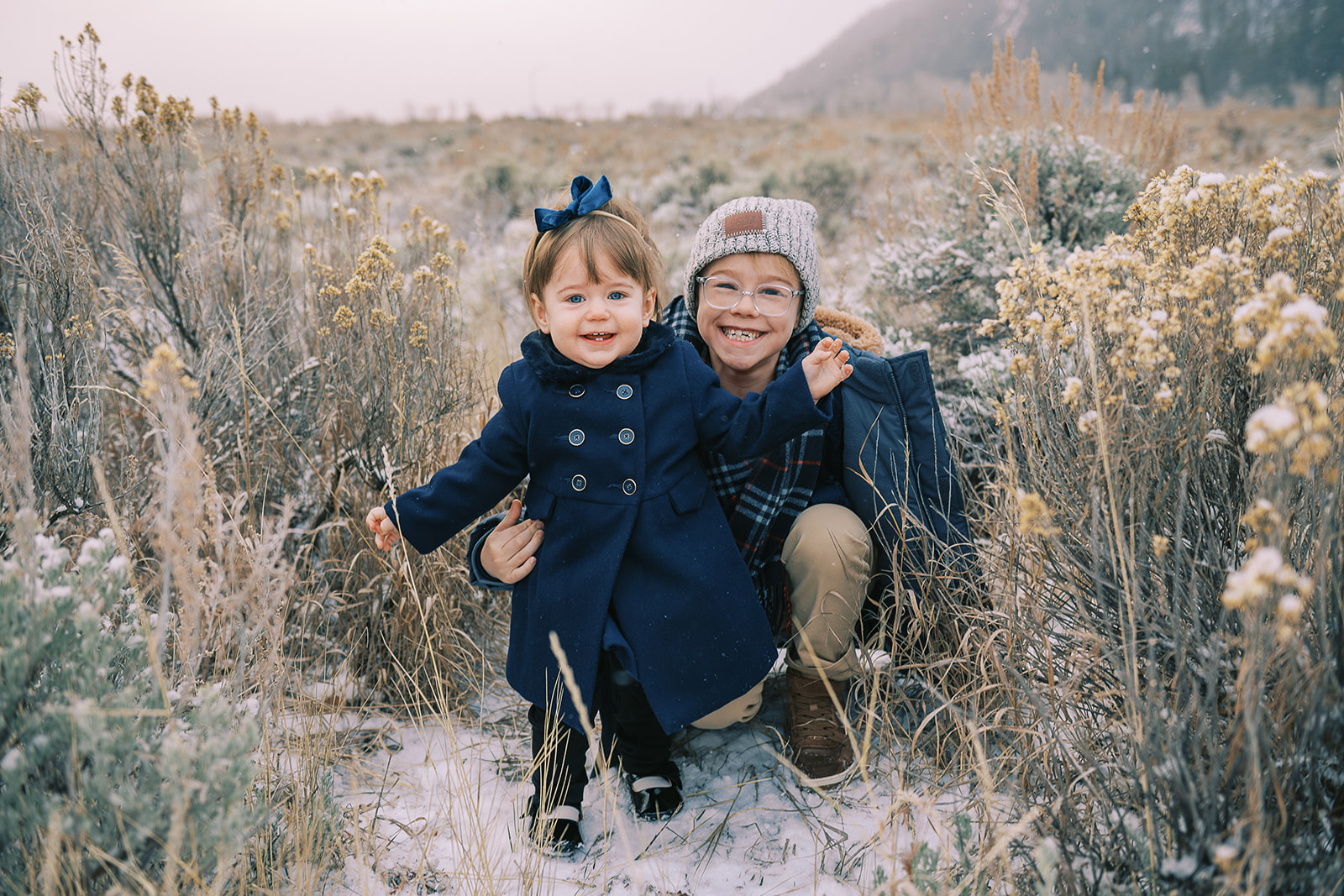 Toddler boy and baby sister in blue in a snow covered meadow