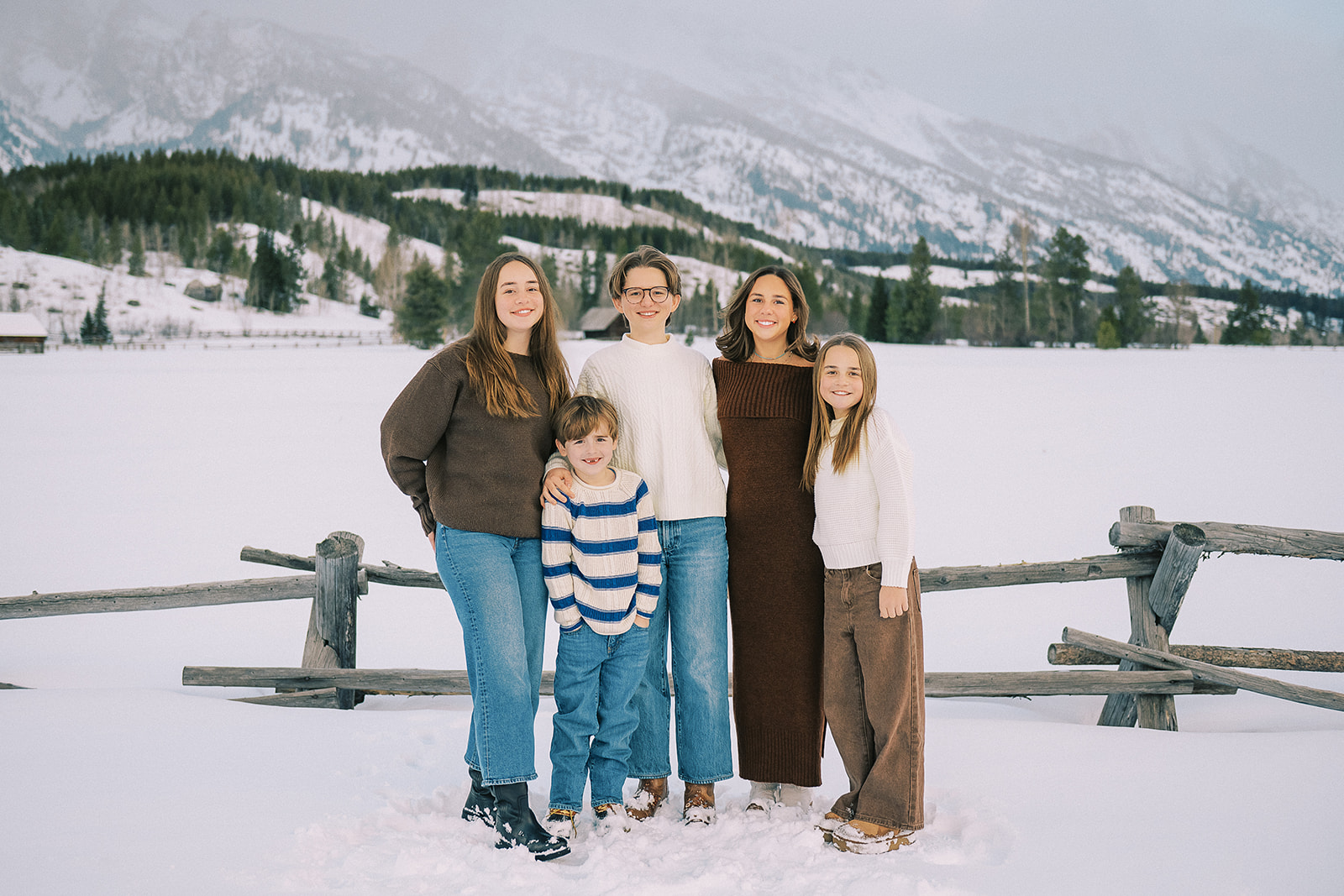 Five cousins stand smiling against a pasture fence with everything covered in snow
