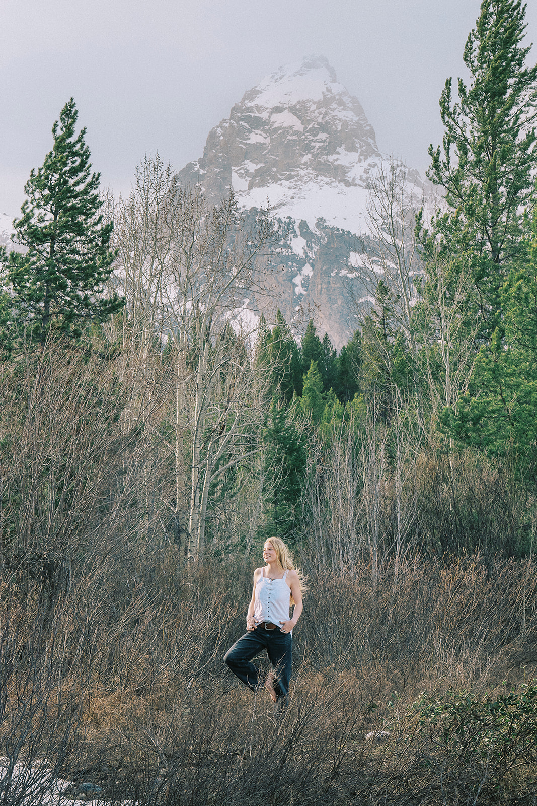 A woman in a white blouse and black pants walks in a forest with a big smile
