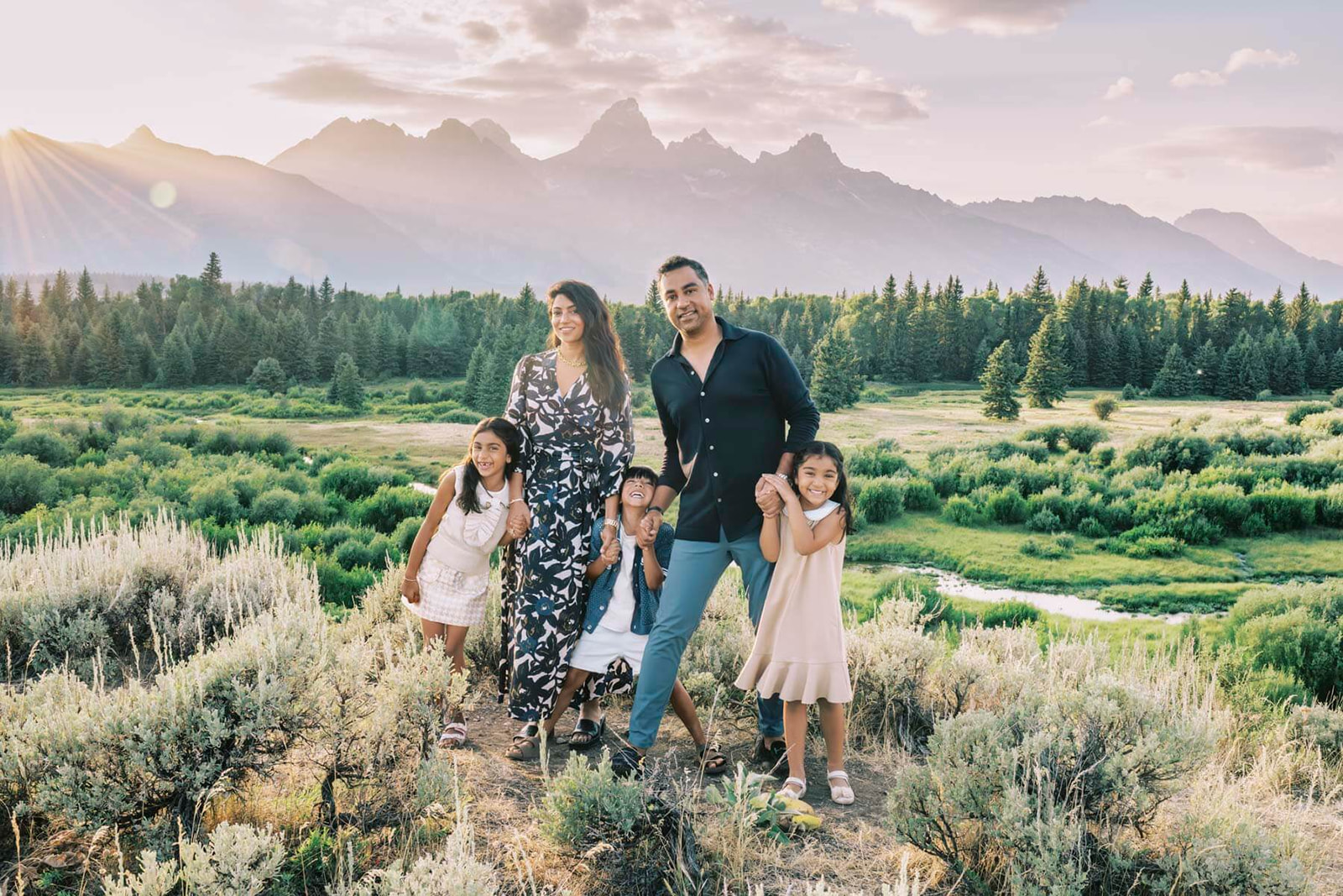 A mom and dad hold hands with their three giggling children at sunset while on a hike in the Grand Tetons