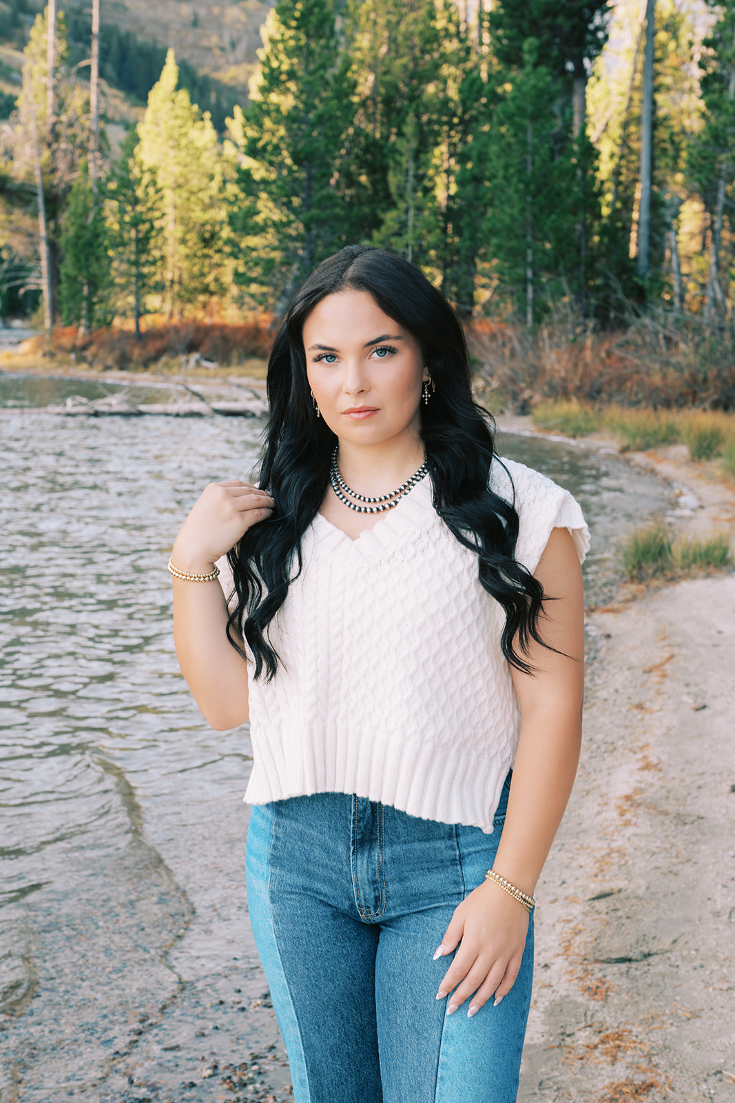 A woman in a white blouse stands near a river while on a hike