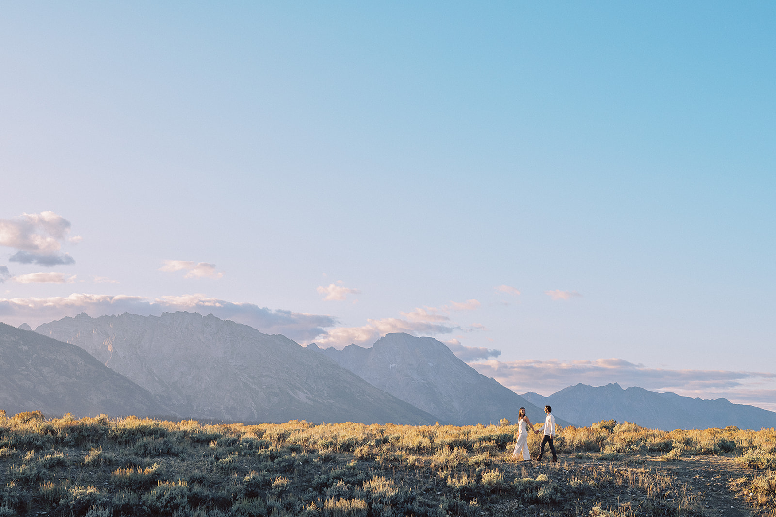 A woman in white leads her partner by the hand on a trail in the national park before heading to romantic restaurants in Jackson Hole