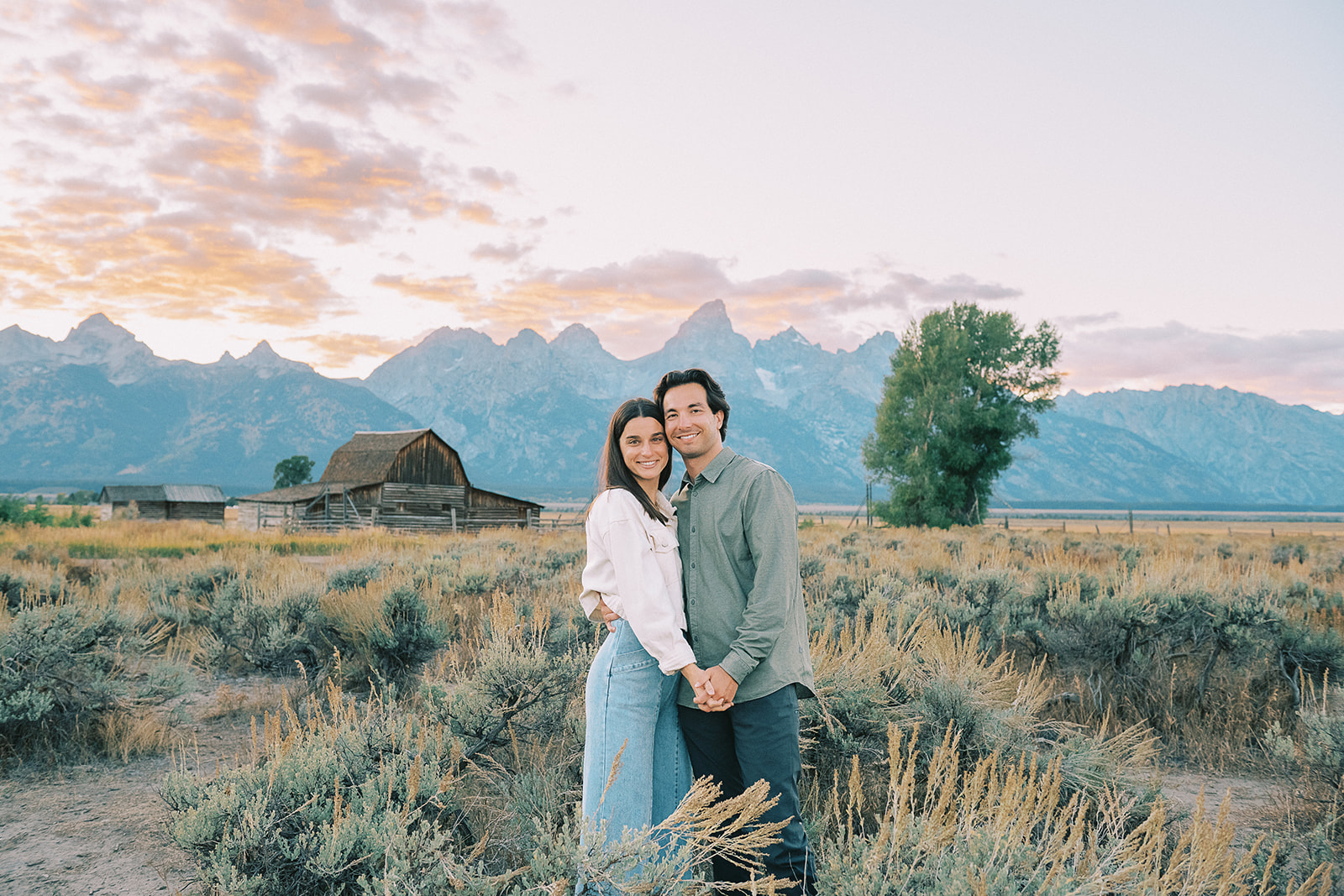 A happy couple stand cheek to cheek in a Grand Teton pasture after finding romantic restaurants in Jackson Hole