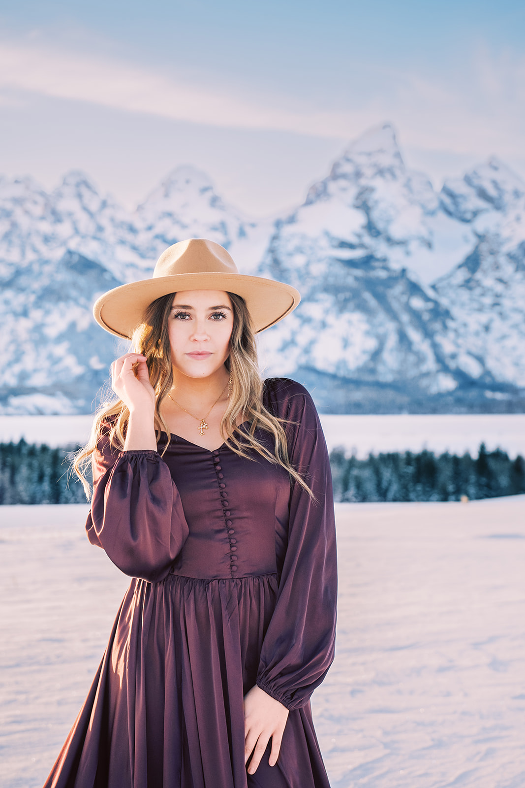 A high school senior in a purple dress plays with her hair in a snow covered field for some senior portraits in Jackson Hole