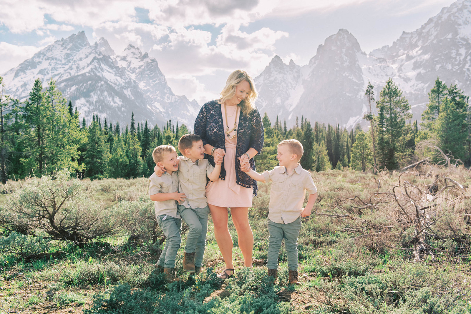 A happy mom walks holding hands with her three toddler sons in matching outfits near the mountains