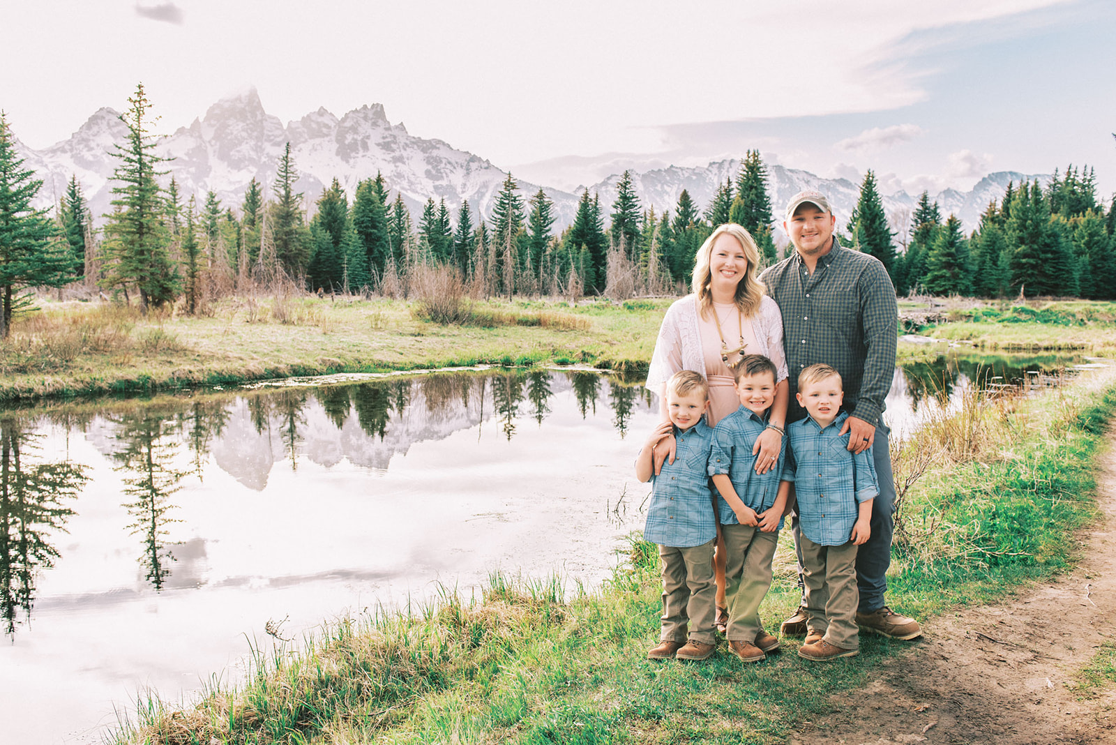 A happy mom and dad stand by a pond with their three matching toddler sons at their feet during things to do in spring in Jackson Hole