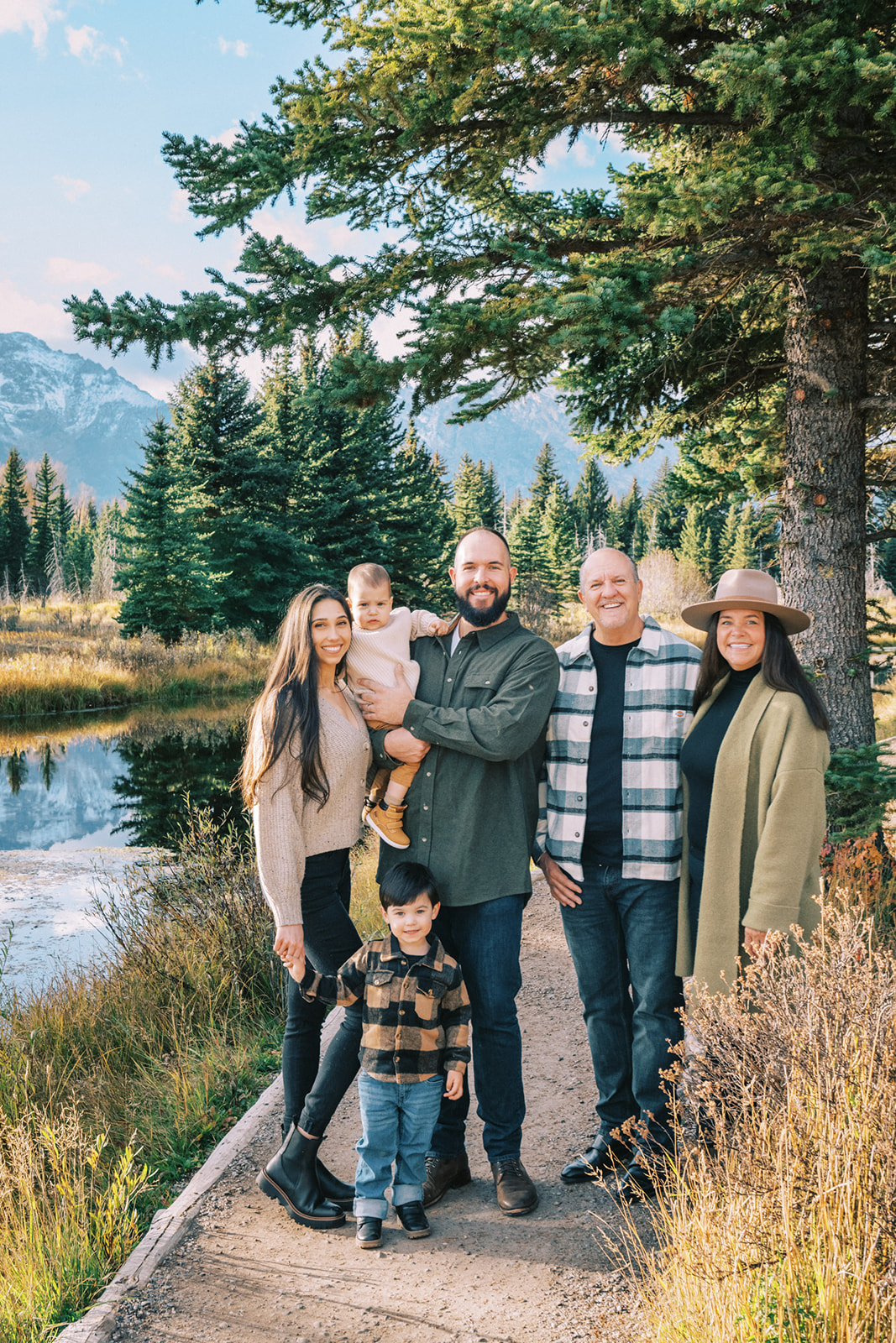 A happy family coordinated in earth tone outfits stand smiling in a mountain trail along a river at sunset after learning what to wear for family photos