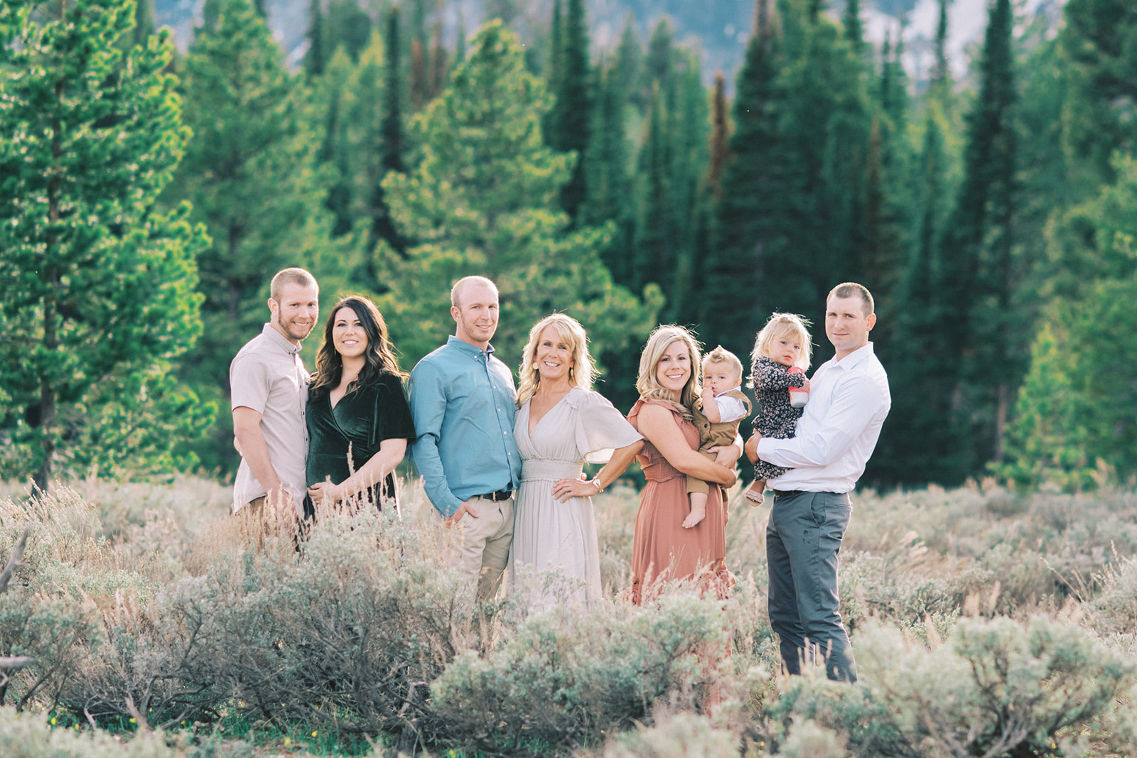 A smiling extended family stands in a forest meadow in tall grass in coordinated outfits after mastering what to wear for family photos
