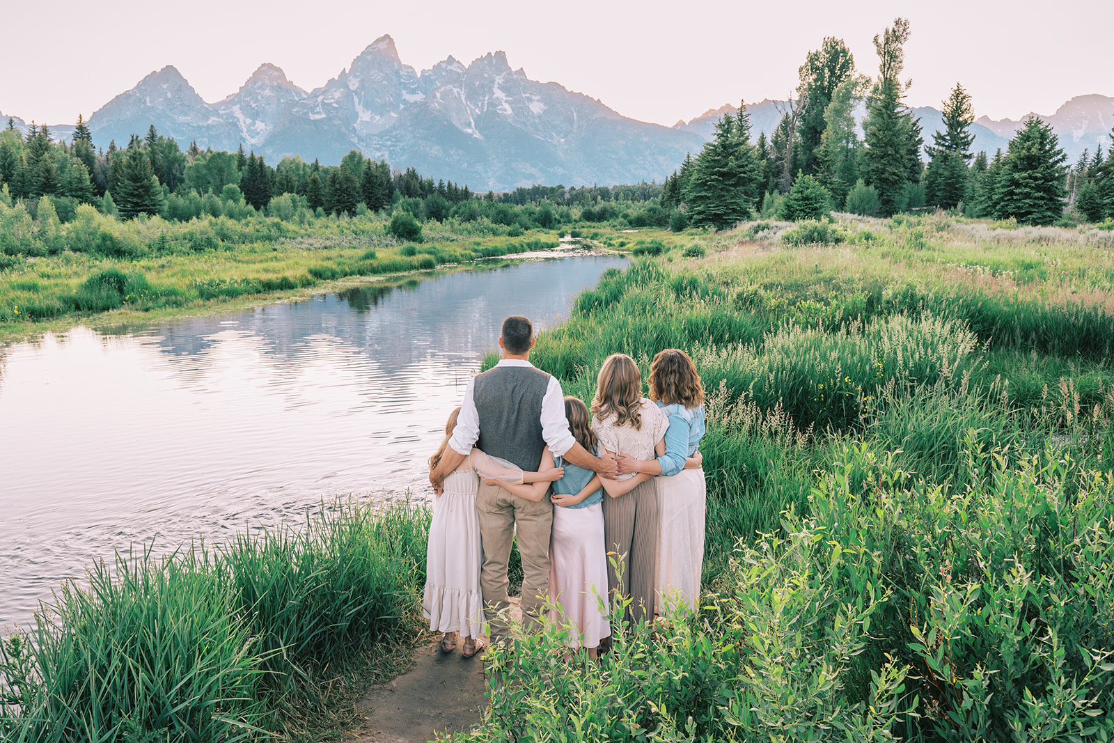 A happy family watches the sunset behind the tetons while on a river hike