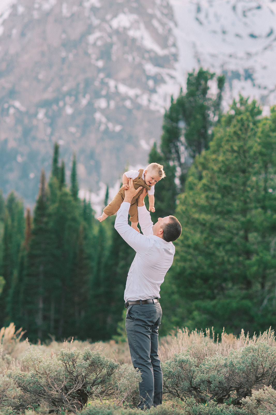A dad tosses his toddler son over his head while on a forest hike at sunset after learning best time to visit Jackson Hole