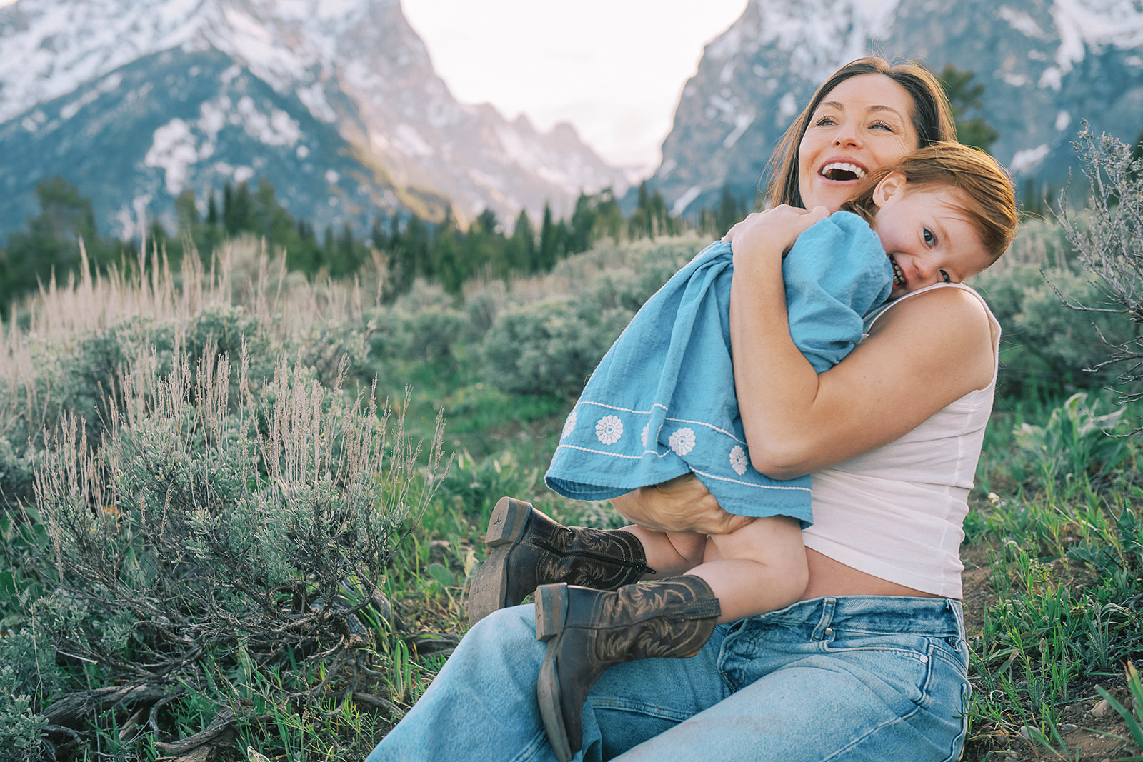 A happy mom plays with her toddler daughter in a meadow after visiting children's boutiques in Jackson Hole