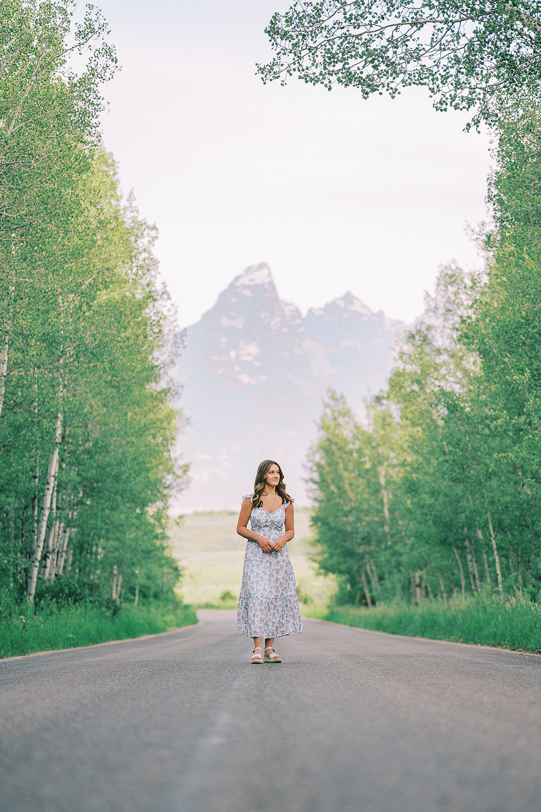 A happy high school senior walks in a rural street in a floral print dress admiring the birch trees after finding college scholarships in Jackson Hole