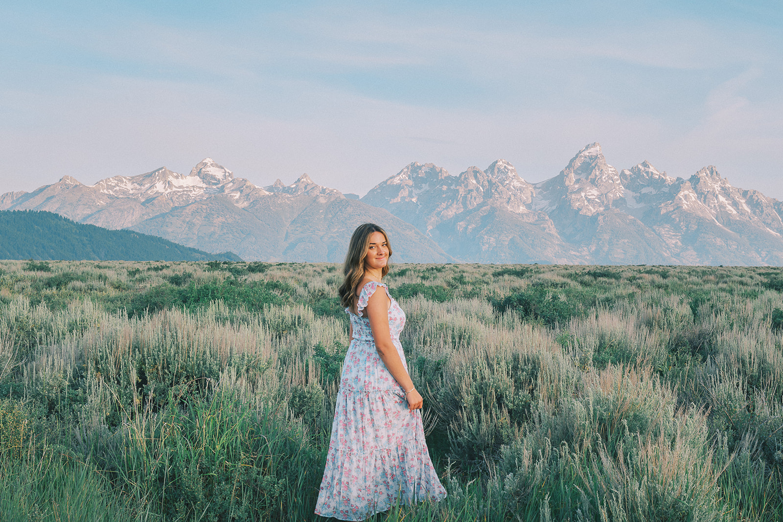A happy high school senior who took advantage of college scholarships in Jackson Hole walks in a meadow in a floral dress at sunset