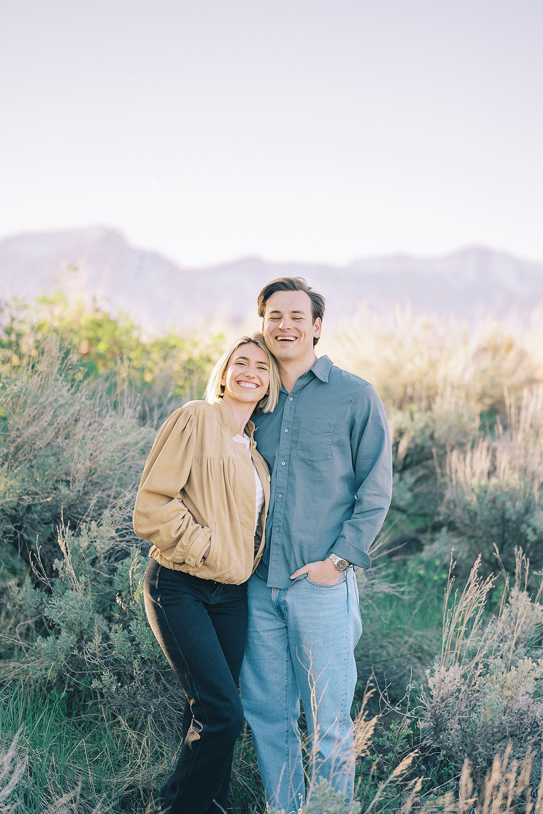 A happy couple snuggles and laughs while on a hike on a hilltop