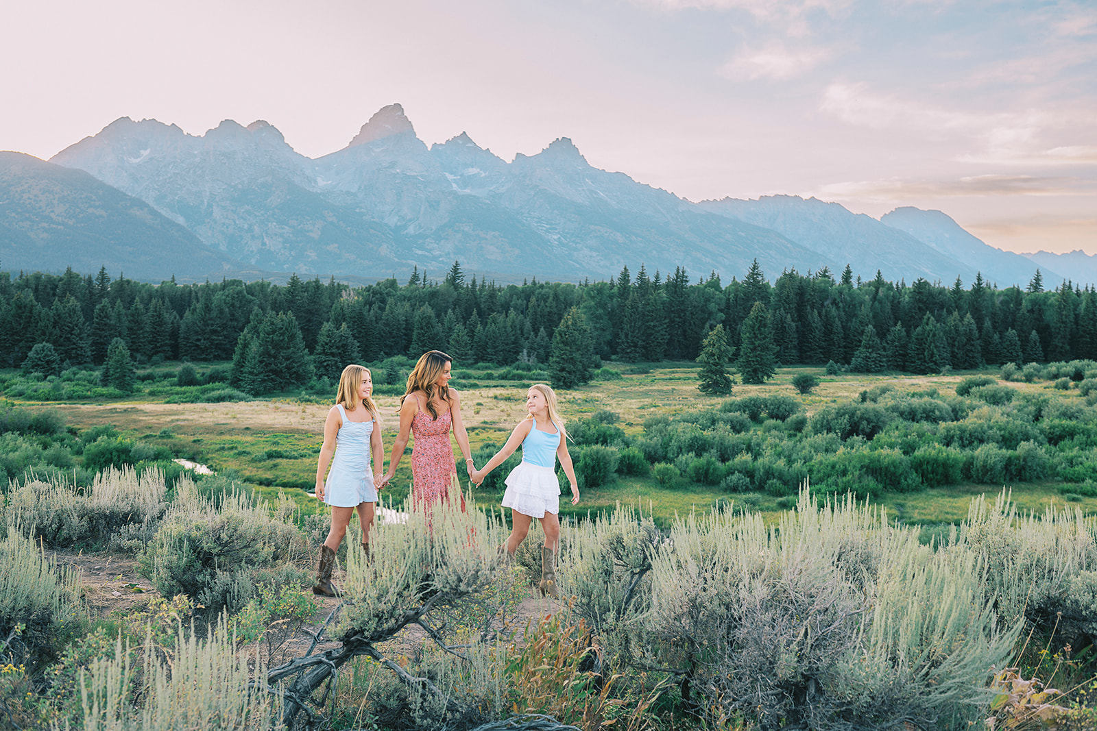A young girl leads her mom and older sister by the hand while on a hike at sunset