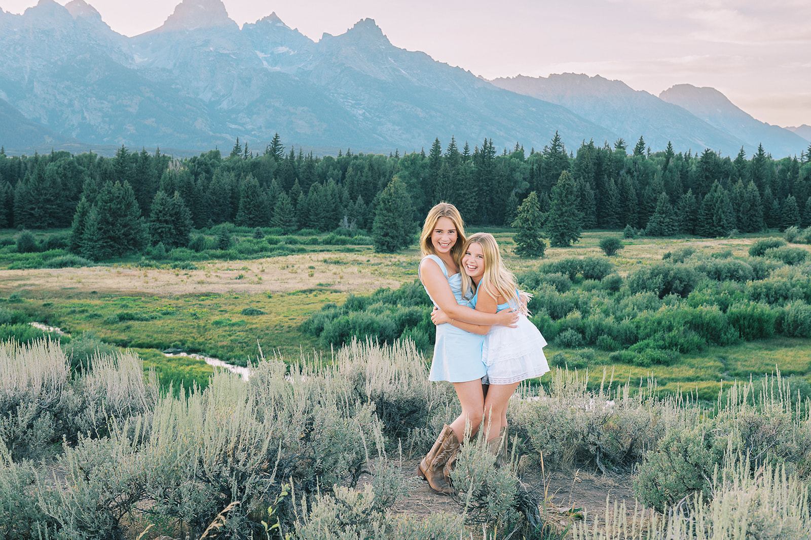 Smiling young sisters in blue and white skirts hug while exploring grand teton national park after finding hair salons in Jackson Hole