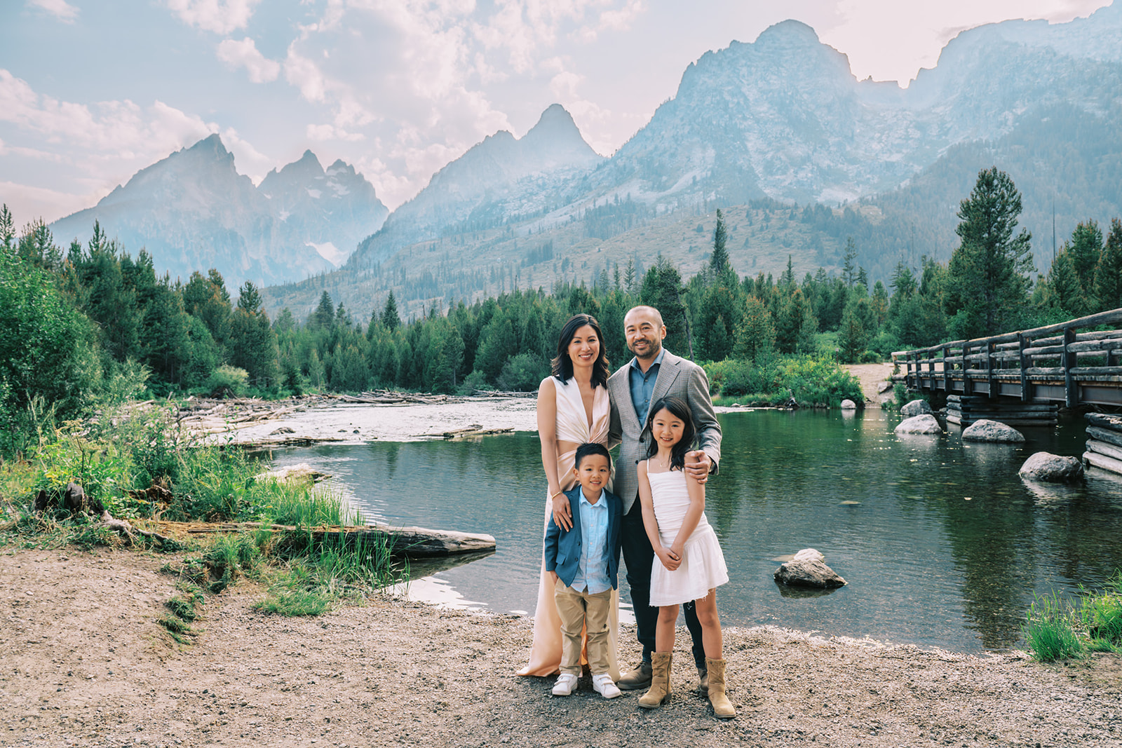 A mom and dad stand on the edge of a river with their young son and daughter in the Tetons
