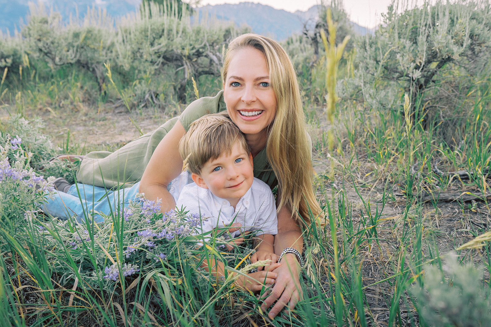 A happy mom snuggles her young son in the grass of a trail