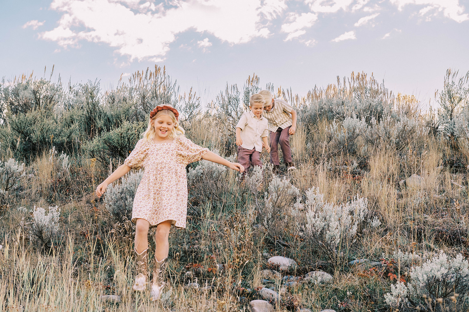 A young girl explores a hillside with her two younger brothers behind her