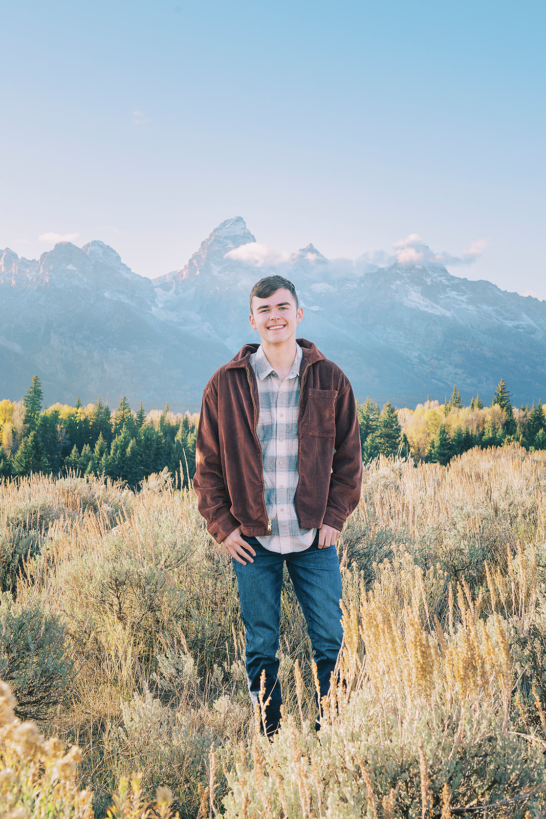 A man walks in a brown jacket through a meadow at sunset with a big smile